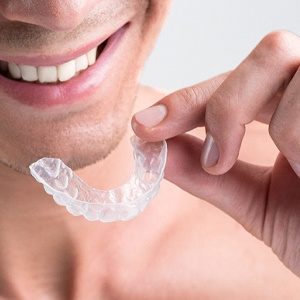 A man smiling while holding an Invisalign aligner
