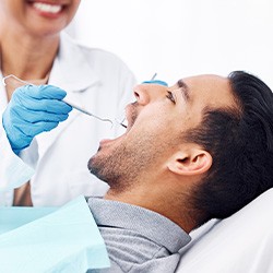 Dentist in white coat and blue gloves examining man’s mouth