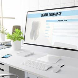 Dental insurance form displayed on computer on white desk with black chair