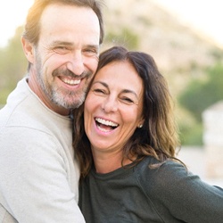 Middle-aged couple smiling in each other’s arms while outside