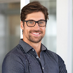 Man with glasses and button-up shirt standing and smiling