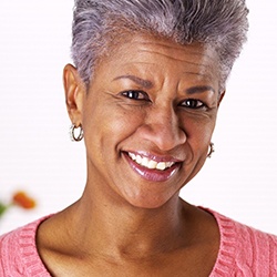An older woman with short hair smiling after receiving her new dentures