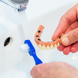 A person cleaning their overdenture with a small toothbrush