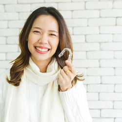 Woman in white sweater holding Invisalign in Horner Glen