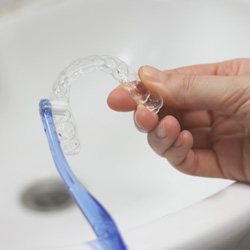 Patient cleaning clear aligner in sink
