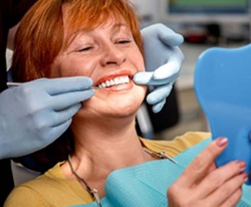 woman looking at her smile in the mirror while sitting in dental chair