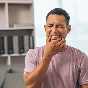 Man in pink shirt squinting touching jaw in pain