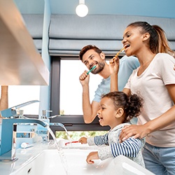 Man, woman, and little girl brushing teeth in blue bathroom