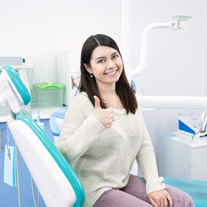 Woman giving thumbs up while sitting in dental chair