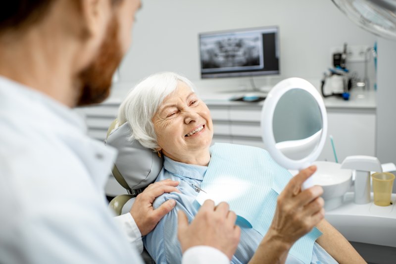 a dentist talking to an older lady who is looking at her new smile in the mirror