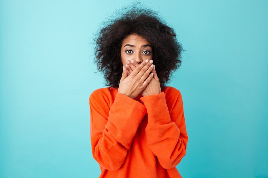 Woman in orange sweater covering her mouth