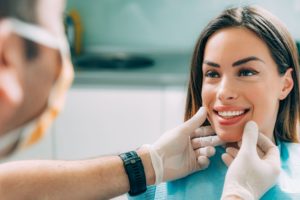 woman with brown hair smiling at dentist who is touching her cheeks with gloved hands