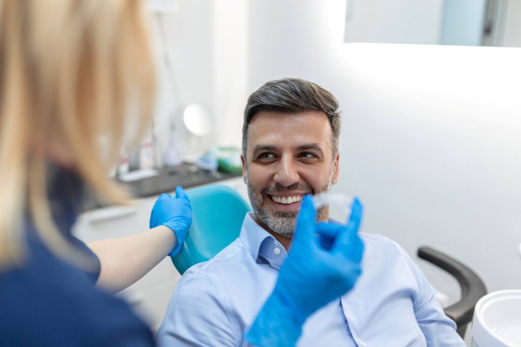 Man smiling at dentist holding clear aligner